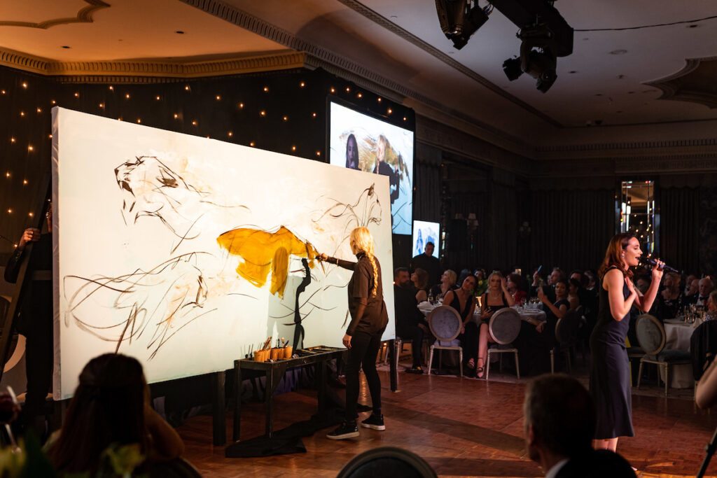 An artist paints flowing images of lionesses, accompanied by music and a singer